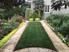 a garden with green grass and flowers in the front yard, next to a house