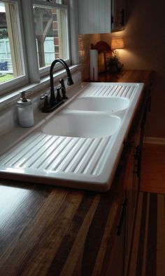 a kitchen sink sitting under a window next to a wooden counter top with two faucets