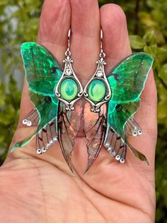 a hand holding a green and silver butterfly broochle with large eyes on it's wings