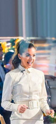 a woman is walking down the street wearing a white shirt and blue pants with her hair pulled back