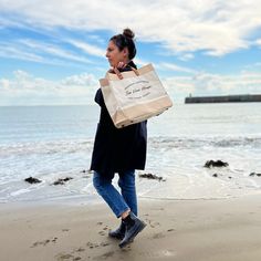 a woman is walking on the beach carrying a shopping bag