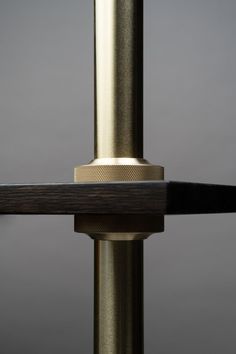 the back end of a metal pole with a black and gold handle on it, against a gray background