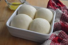 four balls of bread sit in a white dish on a wooden table next to a red and white towel