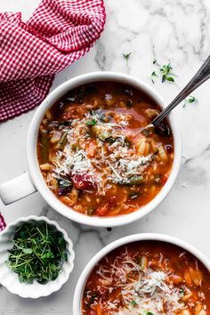 two white bowls filled with vegetable soup and parmesan cheese on the top one