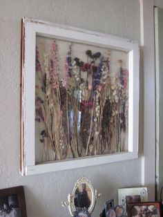 an old window frame with dried flowers in it and pictures on the wall behind it