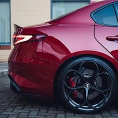 the rear end of a red sports car parked on a brick road in front of a building