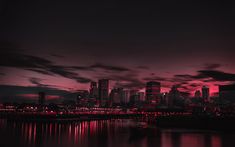 the city is lit up at night with red lights in the sky and reflecting on the water