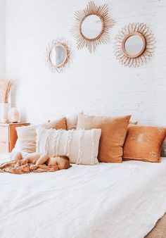 a white bed topped with lots of pillows next to two round mirrors on the wall