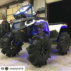 a white and blue four - wheeler is parked in a garage with large black tires