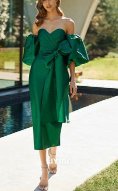 a woman in a green dress is walking down the sidewalk with her hand on her hip