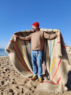 a man standing on top of a sandy beach next to the ocean under a blanket