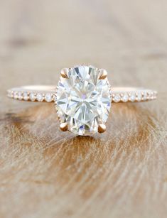 a diamond ring on top of a wooden table with diamonds around the band and an oval shaped center stone