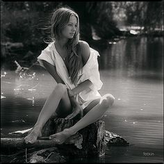 black and white photograph of a woman sitting on a log in the water with her hair blowing in the wind