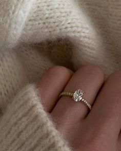 a woman's hand with a diamond ring on her finger, wearing a white sweater