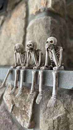 three skeleton figurines sitting on top of a stone wall next to each other