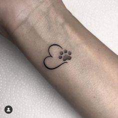 a dog paw and heart tattoo on the left arm, with a black ink outline