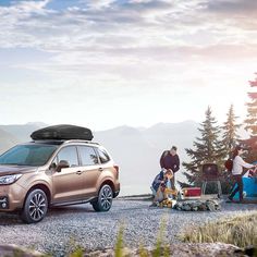 two people sitting on the ground next to a car with a camper in the background