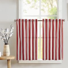 a red and white striped curtain hanging in front of a window next to a vase with flowers