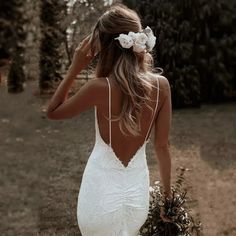 the back of a woman's dress with flowers in her hair, walking down a dirt path