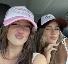 two young women sitting in the back seat of a car, one with her tongue out