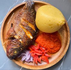 a wooden plate topped with fish next to a lemon and red peppers on a table