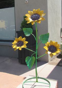 three yellow sunflowers in a green vase on a stand outside the storefront