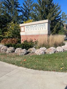 the sign for michigan state university in front of some bushes and trees on a sunny day