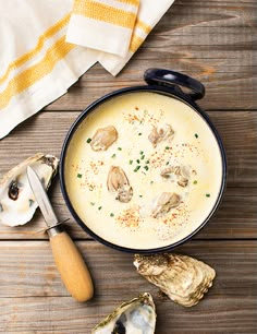 a bowl of soup with oysters and parsley next to it on a wooden table