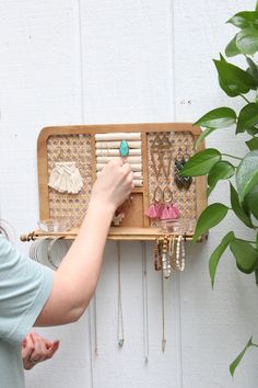 a woman is looking at jewelry hanging on a rack with plants in front of her