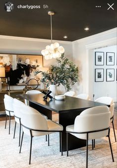 a dining room table with white chairs and a plant in the center is surrounded by pictures on the wall