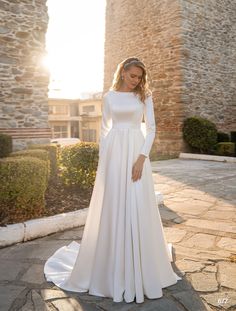 a woman wearing a white wedding dress standing on a stone walkway in front of an old building