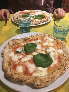 two pizzas sitting on top of a white plate next to glasses and drinking glasses