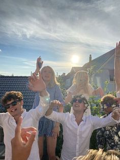 a group of people standing next to each other in front of a house with their hands up