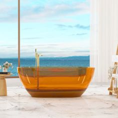 an orange bath tub sitting on top of a marble floor next to a window with the ocean in the background