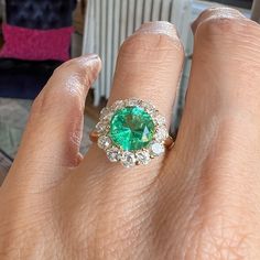 Centering a round faceted emerald weighing approx. 2.24ct., framed by twelve round diamonds 1.10ctw, fashioned in 18k yellow gold. Size 6 3/4. ______ At Doyle & Doyle, jewelry is as sustainable as it is beautiful. Our vintage and antique jewelry is innately ethical and conflict-free as it does not involve any new mining or negative environmental impact. We are proud that our in-house jewelry line Heirloom by Doyle & Doyle is made exclusively for us by our team of expert jewelers in New York City Green Emerald Ring With Rose Cut Diamonds, Green Emerald Cluster Ring With Rose Cut Diamonds, Green Diamond Ring With Rose Cut, Emerald Cluster Ring With Rose Cut Diamonds, Gia Certified Green Cluster Ring, Green Gia Certified Cluster Ring, Green Cluster Ring With Brilliant Cut, Green Brilliant Cut Cluster Ring, Heirloom Green Cluster Ring With Round Cut