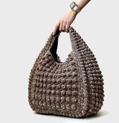 a woman's hand holding a crocheted brown purse on top of a white surface