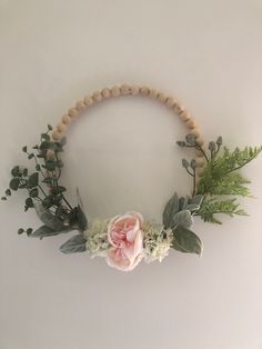 a wooden beaded wreath with flowers and greenery hanging on the wall above it