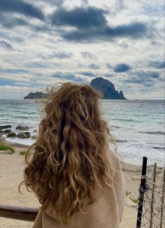 a woman standing on top of a beach next to the ocean with her hair blowing in the wind