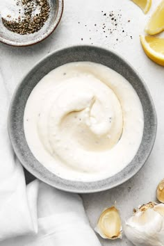 a bowl filled with white sauce next to garlic and lemon wedges