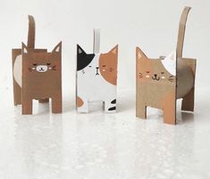 three paper cats standing next to each other on a white surface and one cat has its eyes closed