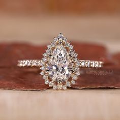 an engagement ring with a pear shaped diamond surrounded by smaller round diamonds on a wooden surface