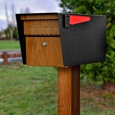 a mailbox in the middle of a grassy area with trees and bushes behind it