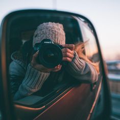 a woman taking a photo in the side mirror of a car with her camera attached