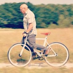 an older man riding a bike in the grass with trees in the backgroud