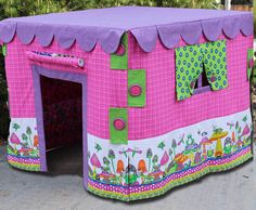 a pink and purple house with lots of decorations on the side walk next to some bushes