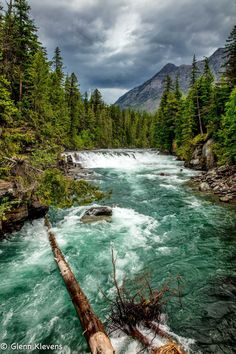 a river with rapids and trees on both sides under a cloudy sky in the mountains