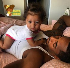 a man laying on top of a bed next to a baby in a white shirt