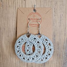 two crocheted circular earrings are hanging from a card on a wooden table with a tag attached to it