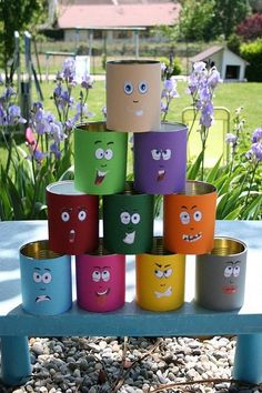 some paper cups with faces on them sitting in the middle of a gravel area next to purple flowers