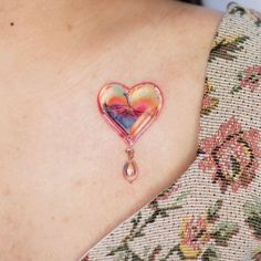 a woman with a heart shaped tattoo on her shoulder and chest is wearing a colorful necklace